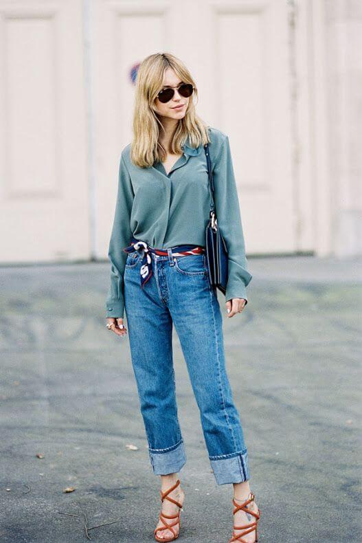 Light olive-green blouse paired with high-waisted blue jeans, strappy tan heels, and a stylish scarf for a chic summer look.