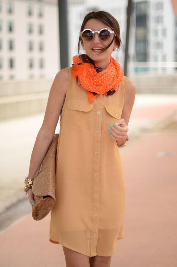 Pale yellow sleeveless summer dress with a button-down front, accessorized with an orange polka dot scarf and large round sunglasses.
