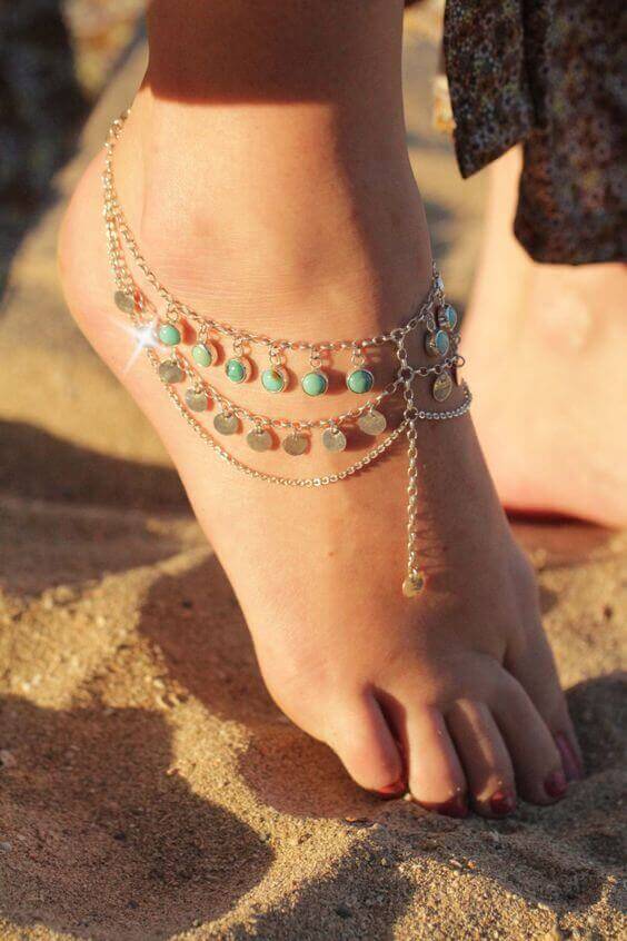 Anklet jewelry with multiple chains, turquoise stones, and circular charms, draped elegantly in a sunlit, sandy setting, embodies boho style.