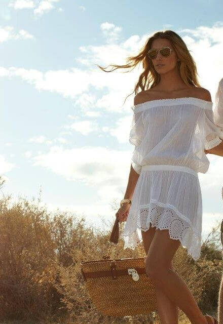 Off-shoulder white summer dress with lace trim, styled with large sunglasses and a woven straw basket, perfect for beach outings.
