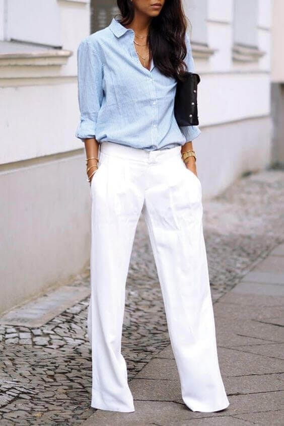 Light blue vertically striped shirt with fitted cut, high-waisted white wide-leg trousers, gold bracelets, and black clutch. Perfect summer business casual look.