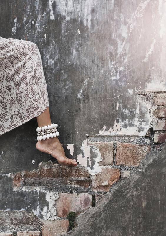 Delicate ankle bracelet adorns a bare foot on rugged exposed bricks, showcasing a bohemian vibe against a weathered backdrop.