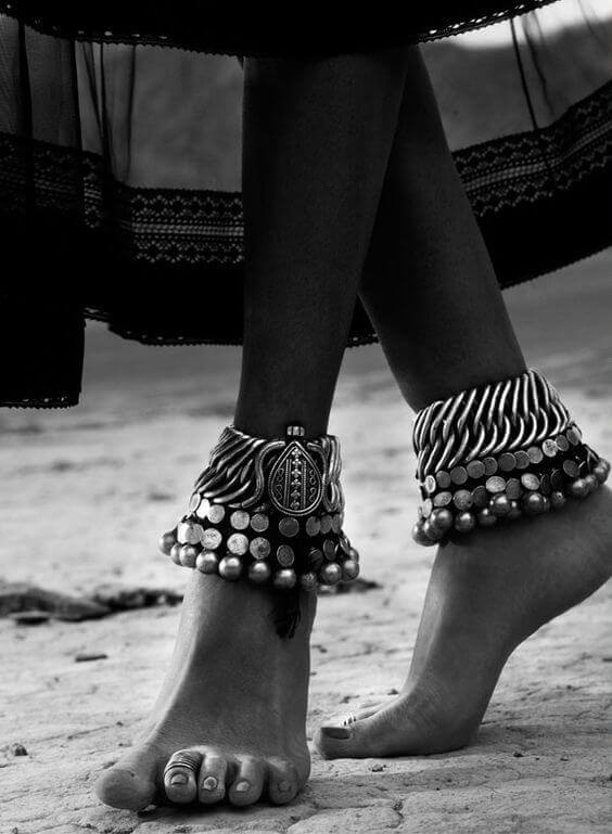 Anklets with intricate silver detailing and large coins, layered design, set against a sandy outdoor backdrop, showcasing boho style.