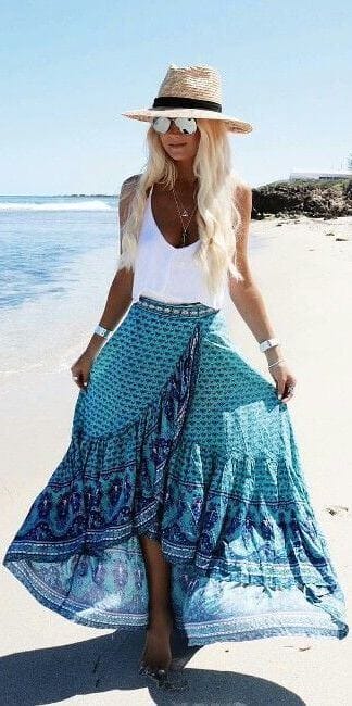 Ankle-length bohemian skirt in vibrant turquoise and blue, paired with a white tank top, straw hat, and sunglasses for a beach setting.