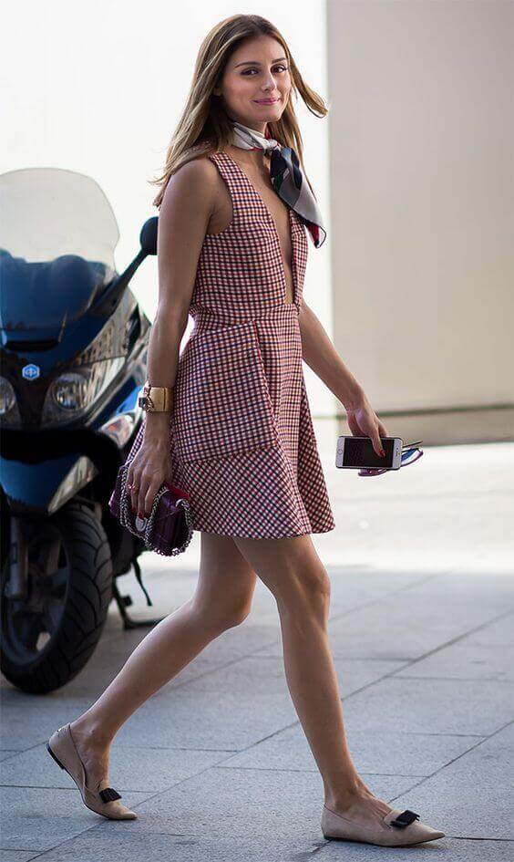 Red and white gingham dress with a deep V-neckline, flared skirt, silk scarf, nude flats with a black bow, and a small handbag.