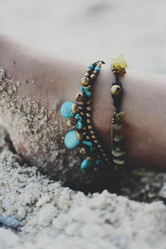 Anklet with turquoise beads, gold accents, and natural stones on a black cord, creating a bohemian, beach-ready look.