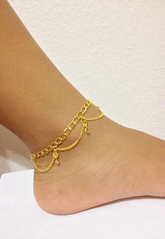 Delicate gold anklet made of layered chains, adjustable for various ankle sizes, adds elegance to summer outfits.
