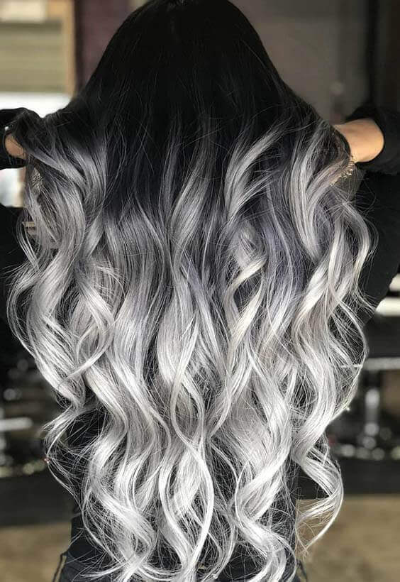 Ombre hairstyle with a gradient from deep black roots to silvery gray tips, featuring mid-back length and soft waves.