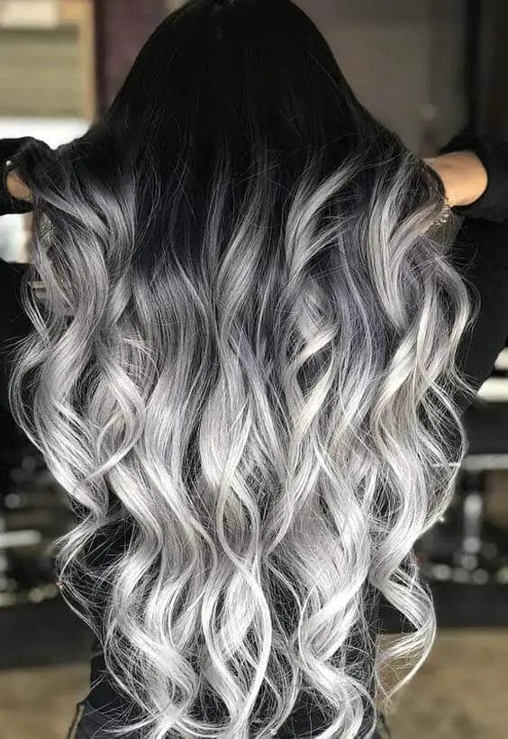 Graceful transition from natural root to shimmering silver waves with layered cut for movement and dimension, paired with loose, tousled curls.