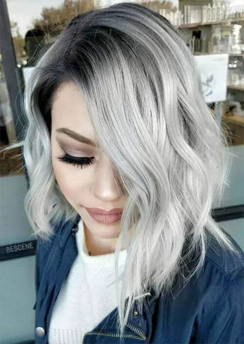 A woman's chic lob hairstyle with natural roots transitioning seamlessly into icy gray highlights, featuring soft layers for movement and a side-parted fringe that frames the face, creating a modern and versatile look.