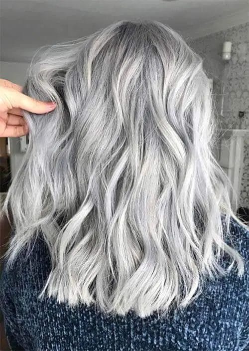 A woman's hair in a luxurious silvery gray shade, cascading in soft, wavy layers that add body and movement to the elegant and contemporary style, perfect for those seeking sophistication with a modern twist.
