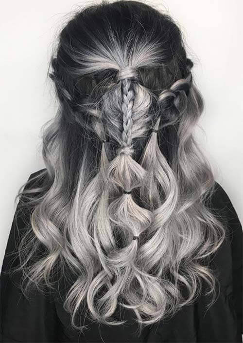 A woman's enchanting hairstyle featuring deep charcoal and luminescent silver strands intricately woven into a delicate fishtail braid at the crown, cascading into rippling waves for a multi-dimensional, ethereal look with a modern twist.
