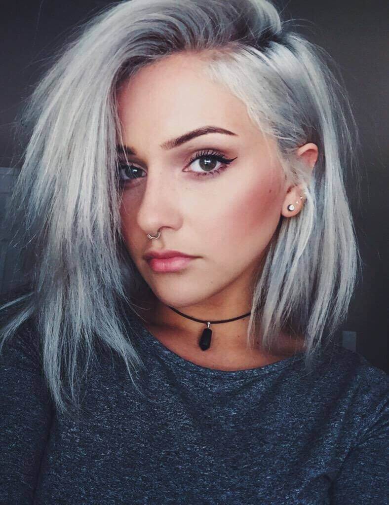 A woman's chic shoulder-length hairstyle with sleek silver hair featuring deeper gray roots for added depth and a touch of edginess, creating a modern and low-maintenance high-impact look with a softening side part.