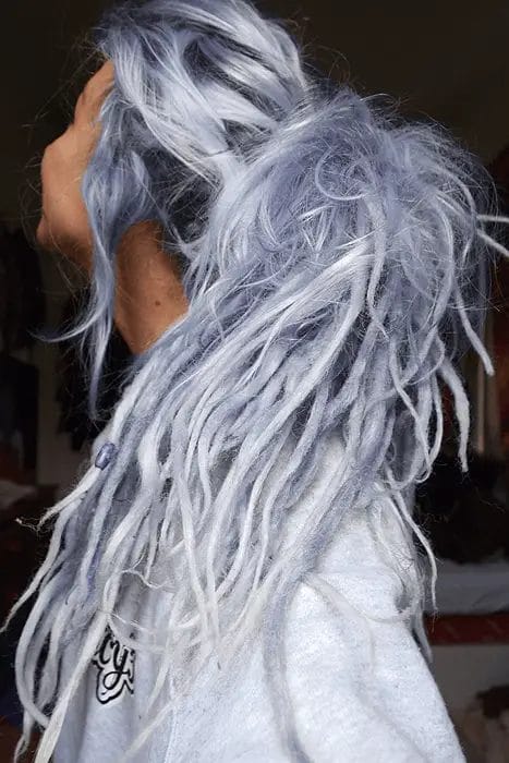 A woman's free-spirited hairstyle featuring cascading dreadlocked tendrils in icy blue and gray hues, with an organic, tousled appearance, varying lengths, and a unique blend of bohemian and modern flair.