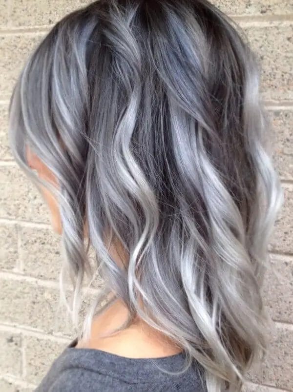 A woman's hair with a harmonious blend of smoky gray and silver highlights, transitioning from deep charcoal roots to silvery ends, featuring soft, flowing layers that add dimension and movement.