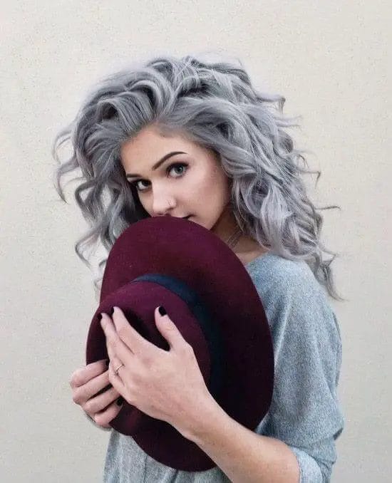 Voluminous silver-gray curls with subtle lavender undertones, playful waves, and a loose, side-swept fringe, creating a romantic and dreamy hairstyle with a touch of youthful energy.