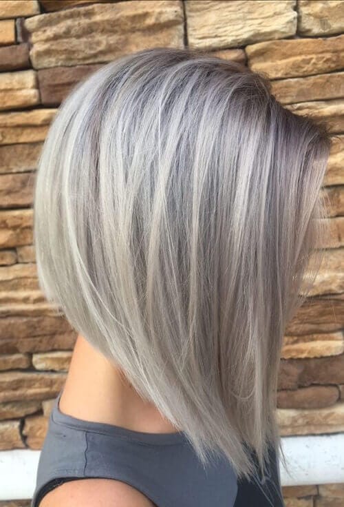 A woman's sleek bob featuring smoky gray highlights seamlessly blending into a silvery base, with polished, feathered layers framing the face and a silky smooth finish.