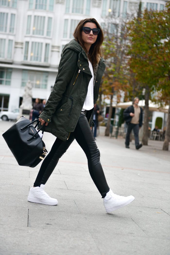Casual outfit with a long green parka, white knit top, black leather skinny jeans, and white sneakers, perfect for cool climates.