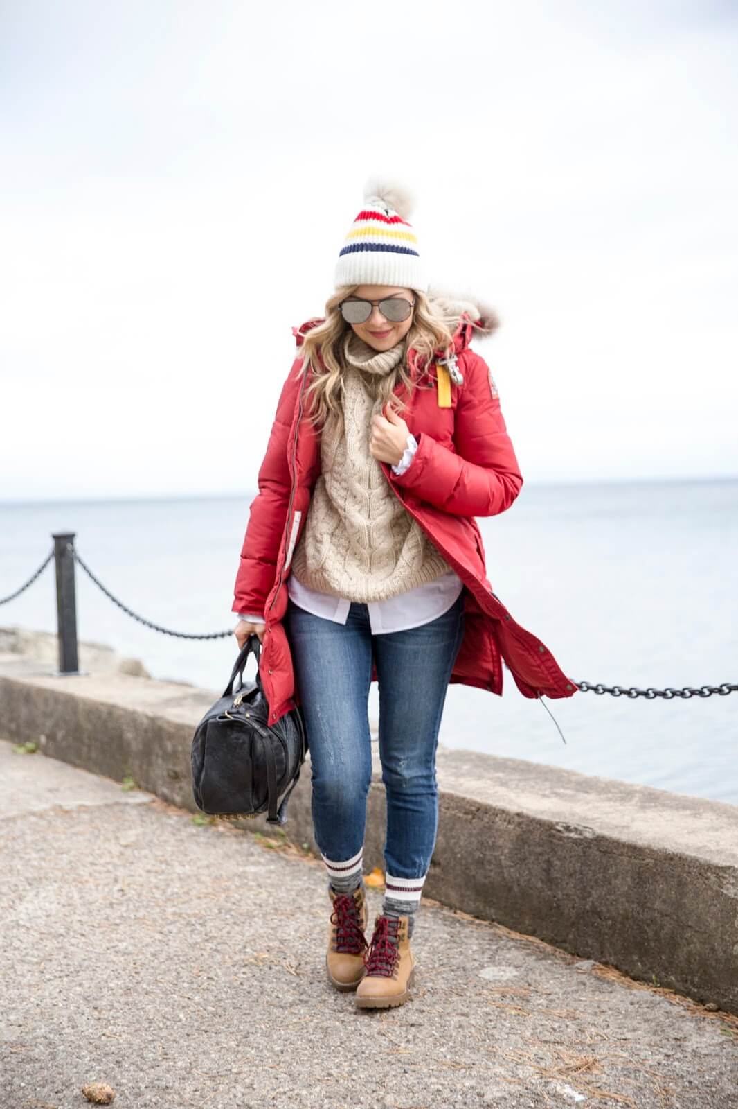 Vibrant red parka jacket layered over a beige knitted sweater, fitted blue jeans, and knee-high tan boots, ideal for cold weather.