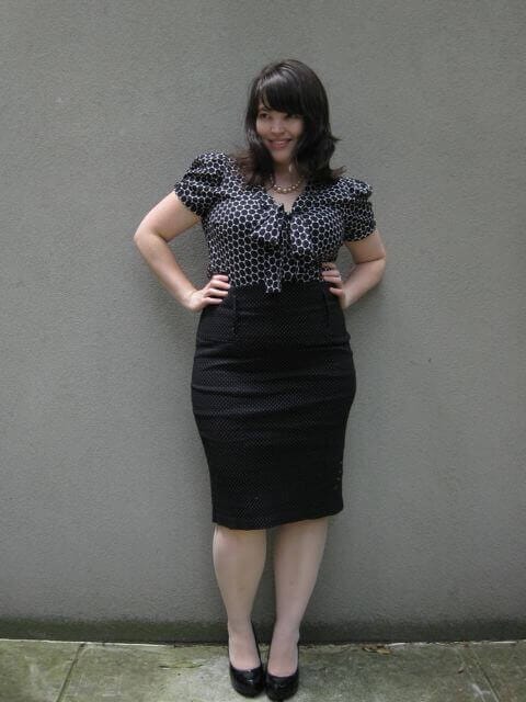 Plus size office outfit featuring a fitted silhouette, short puff sleeves, and a knee-length design in a classic black-and-white polka dot pattern.