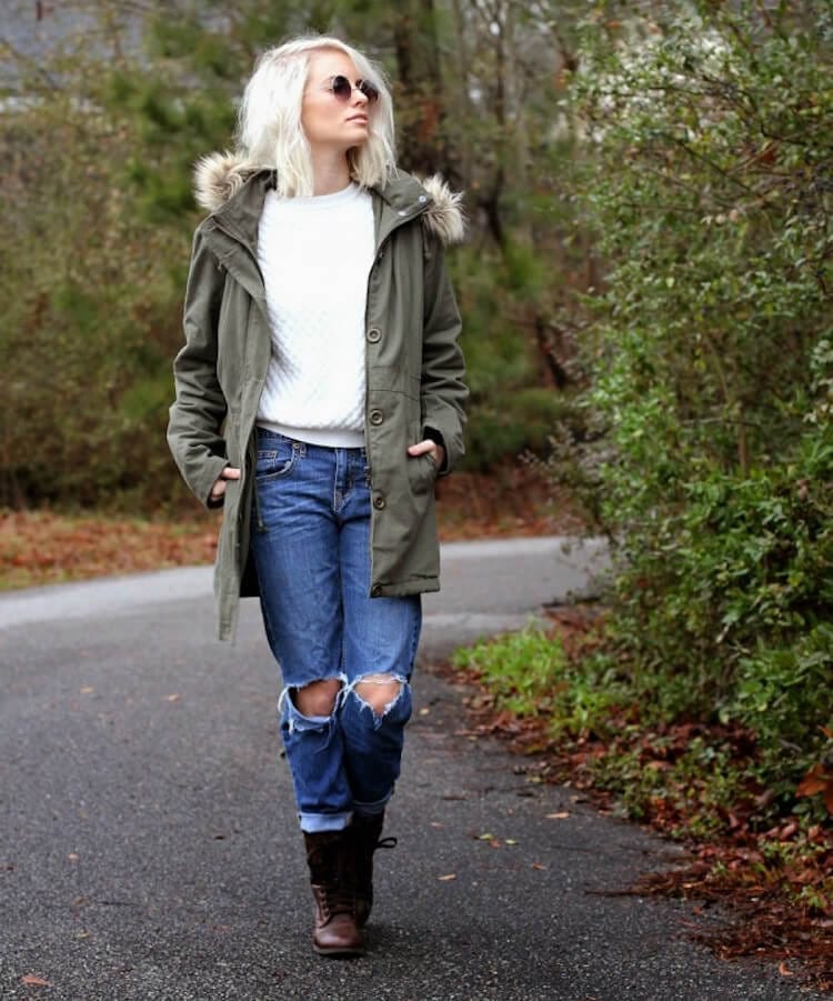 Olive green parka jacket outfit with a fur-lined hood, white cable-knit sweater, distressed denim jeans, and brown lace-up boots.