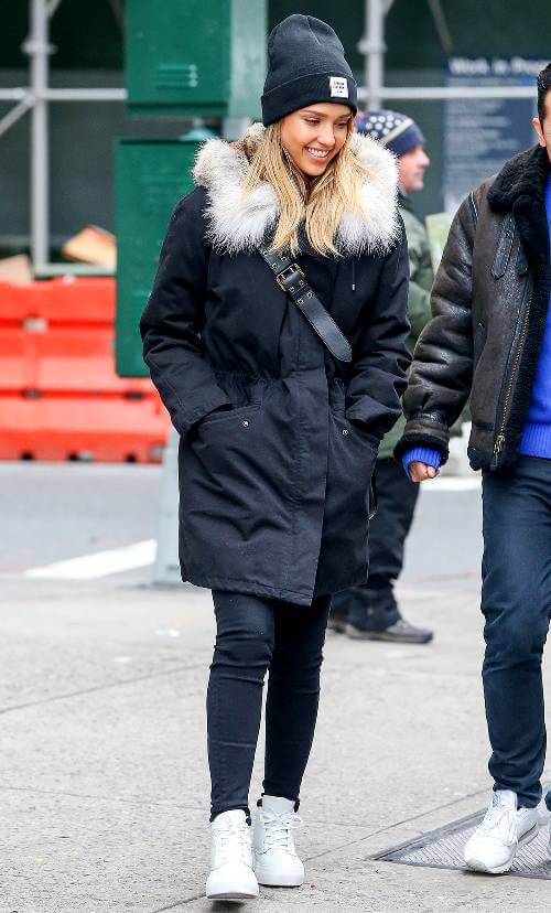 Casual winter outfit with a black parka featuring a fur-lined hood, black jeans, and white sneakers, perfect for urban cold weather.