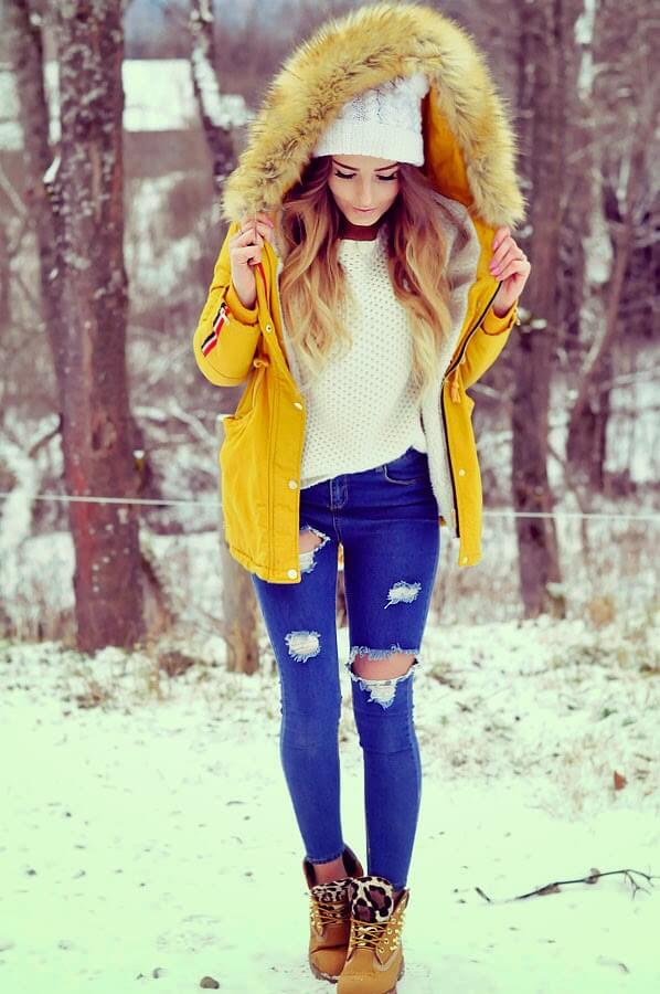 Bright yellow parka with faux fur-lined hood over a white sweater, distressed blue skinny jeans, and tan leopard print boots.