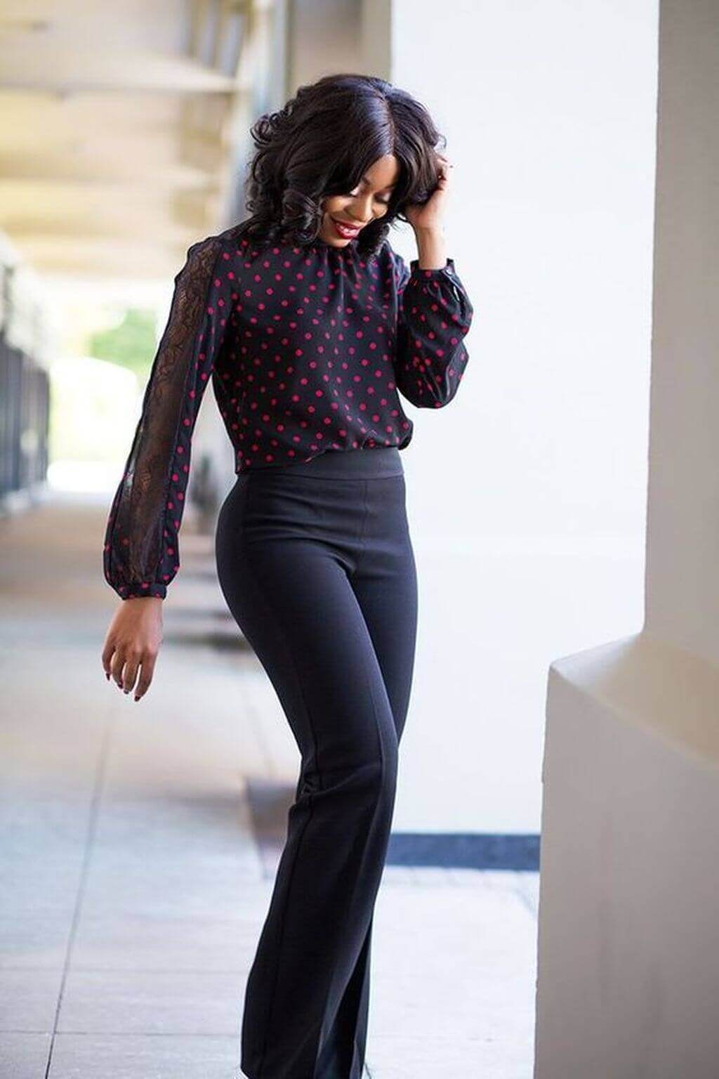 Black polka dot blouse with sheer lace sleeves paired with high-waisted black trousers, ideal for stylish office wear.