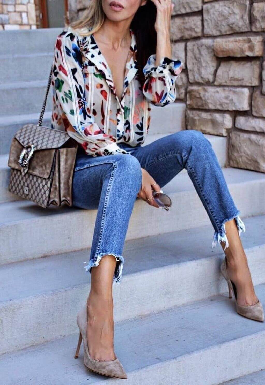 Casual chic outfit with a floral blouse, light-wash distressed jeans, and nude suede heels, styled with a handbag and sunglasses.