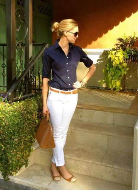 Sleek low bun hairstyle with minimal accessories, paired with a smart dark shirt and white pants in an outdoor setting, reflecting sunlight.