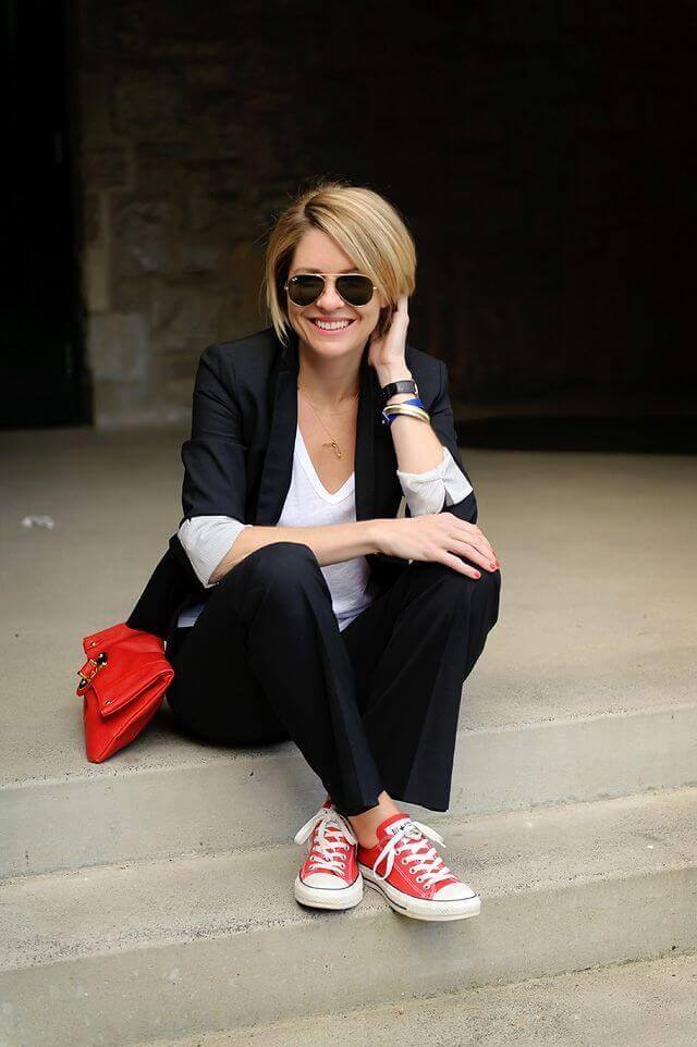 Casual office attire features a fitted black blazer over a white top, tailored black trousers, and red converse shoes, styled outdoors.