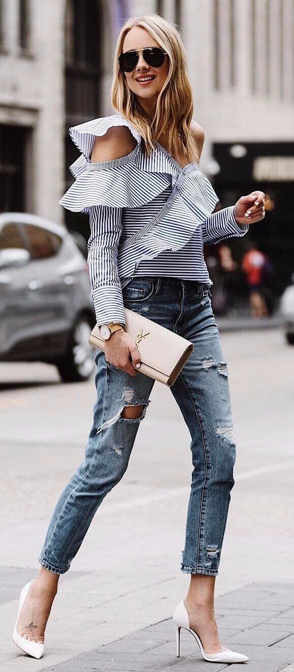 Stylish off-the-shoulder striped blouse paired with distressed blue jeans and white stiletto heels, embodying casual office attire for women.