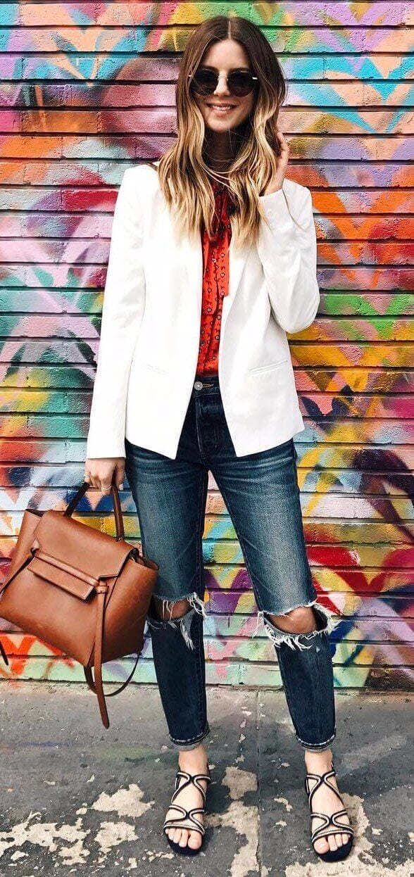 Long, wavy hair styled with volume complements a tailored white blazer and distressed jeans, embodying casual office attire for women.