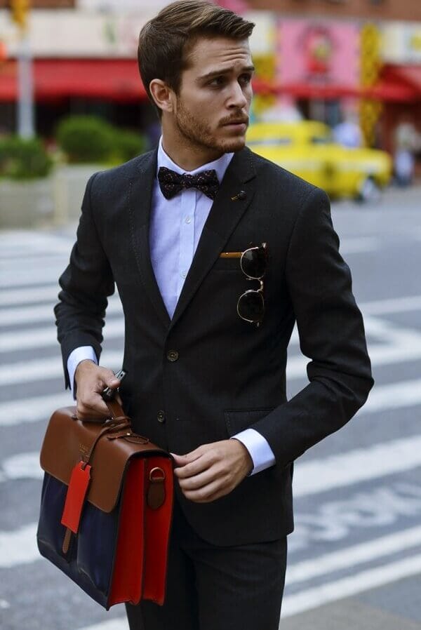 Fitted dark suit with a white shirt, patterned bow tie, and sunglasses on the lapel, perfect for formal urban occasions.