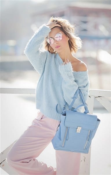 Light blue off-shoulder fluffy sweater paired with pink high-waisted trousers. Accessorized with mirrored sunglasses and a light blue handbag.