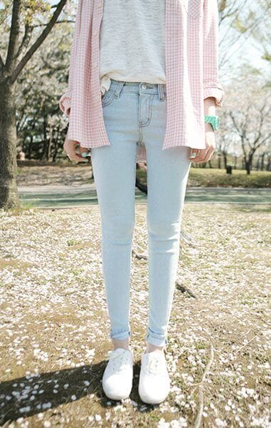Light blue skinny jeans with a loose gray shirt layered under a pink gingham button-up, paired with white sneakers. Cherry blossoms surround the outfit, perfect for spring.