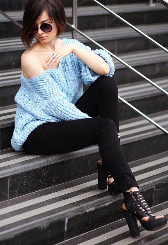 Chic tousled bob hairstyle with natural volume, paired with a light blue oversized sweater and black skinny jeans, set against grey stone steps.
