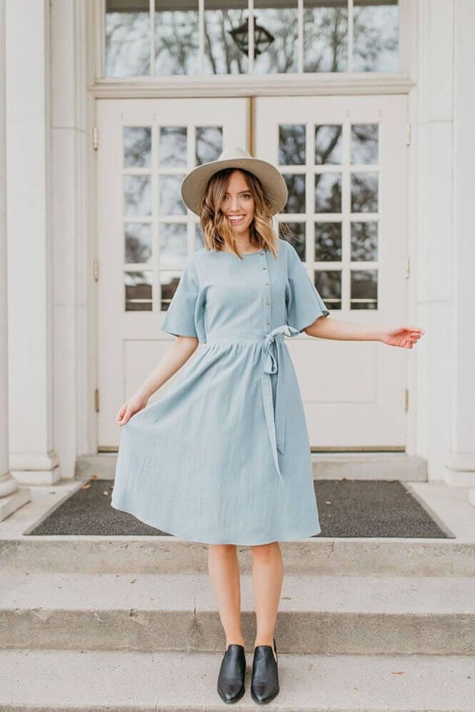 Light blue A-line dress made of soft linen, featuring a fitted waist, short sleeves, and button-down front, styled with black ankle boots.