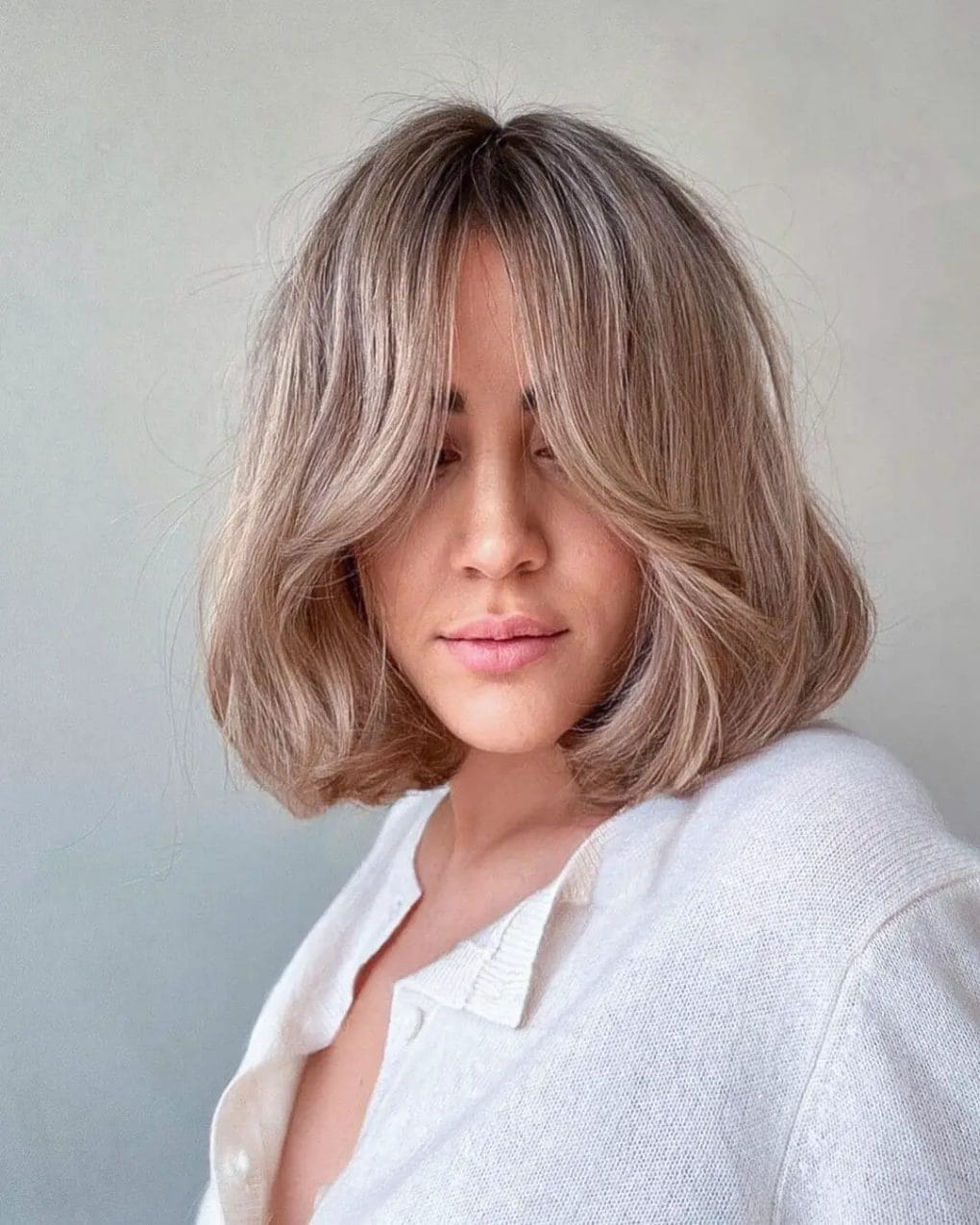 Layered cut with ashy blonde tones and fringe.