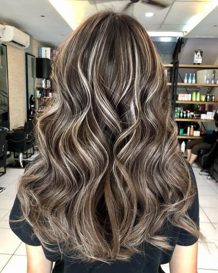 Beige balayage blending dark base with warm and cool highlights, styled in long layers with waves