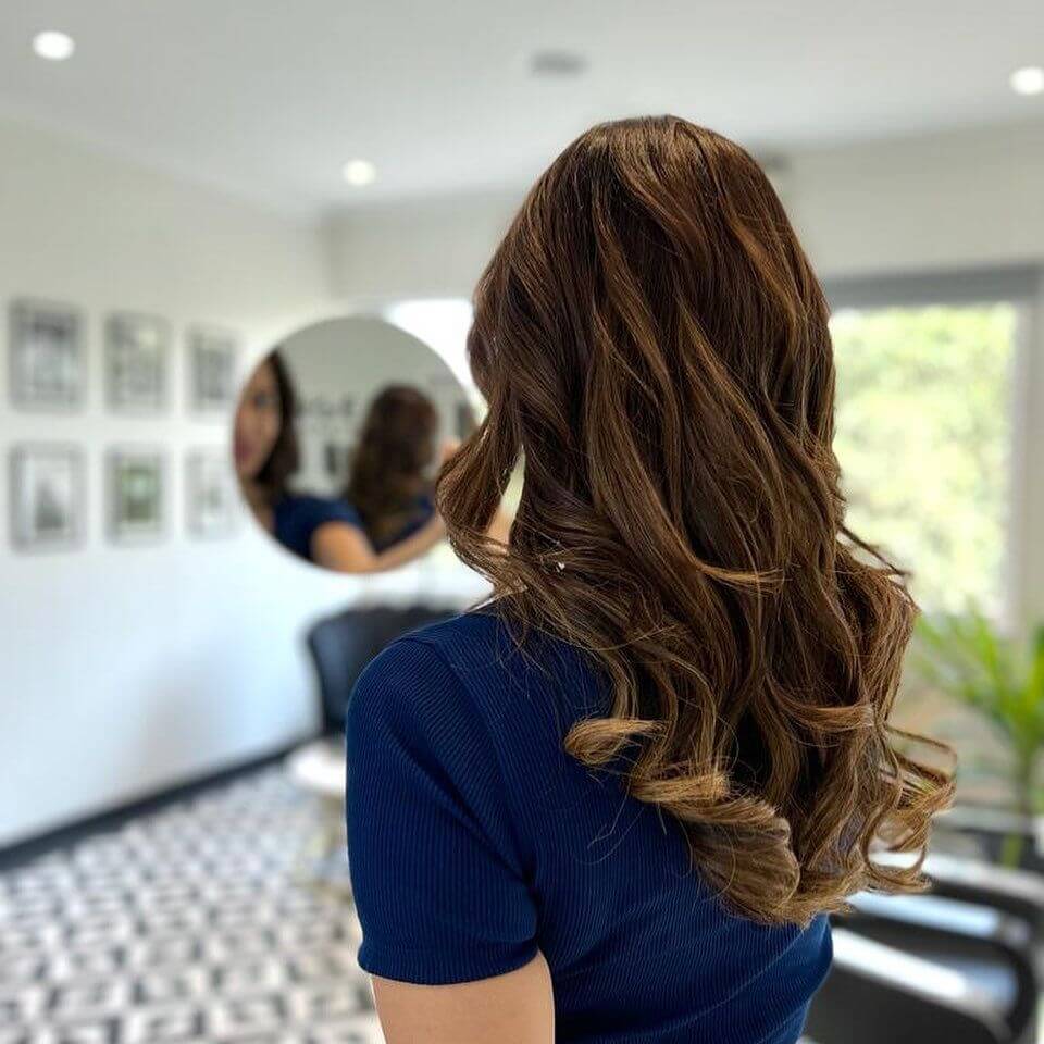 Chocolate brown with caramel balayage highlights, styled in long layers ending in soft curls