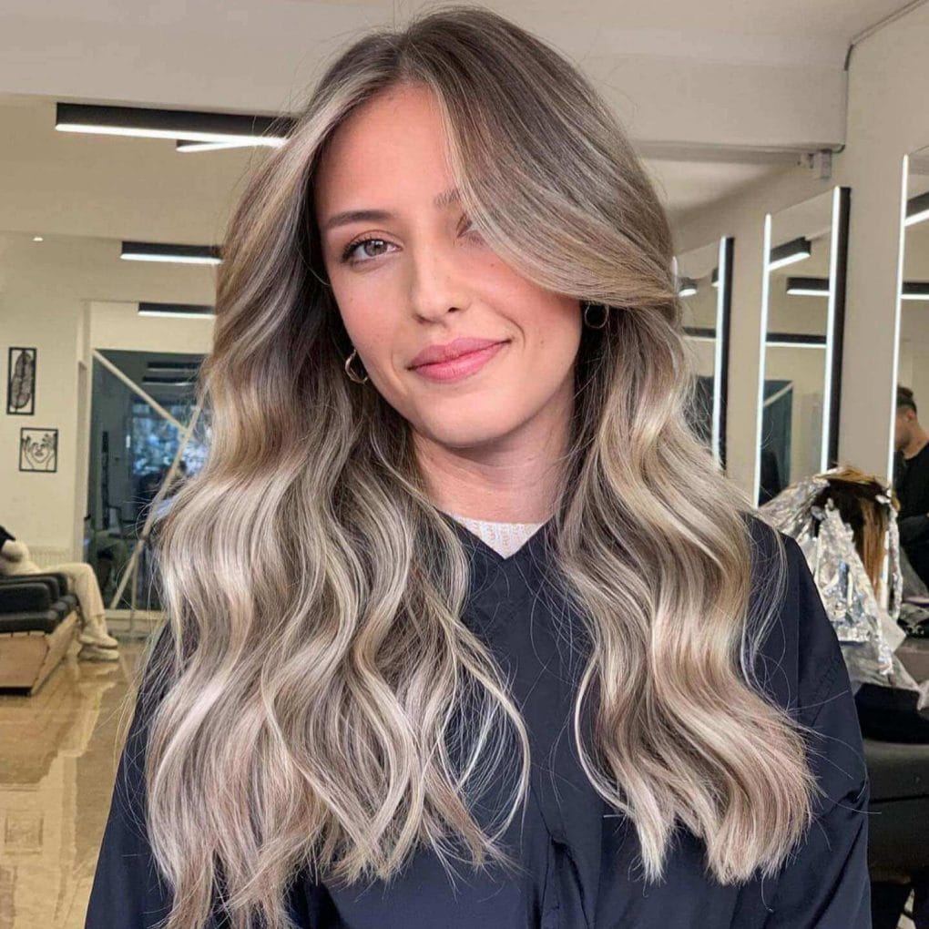 Ash tones at the root transitioning into bright blonde waves, long flowing layers adding movement