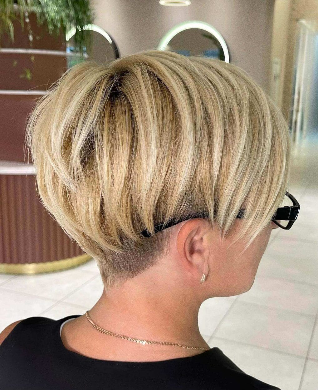 Blonde balayage pixie with undercut and razored bangs.