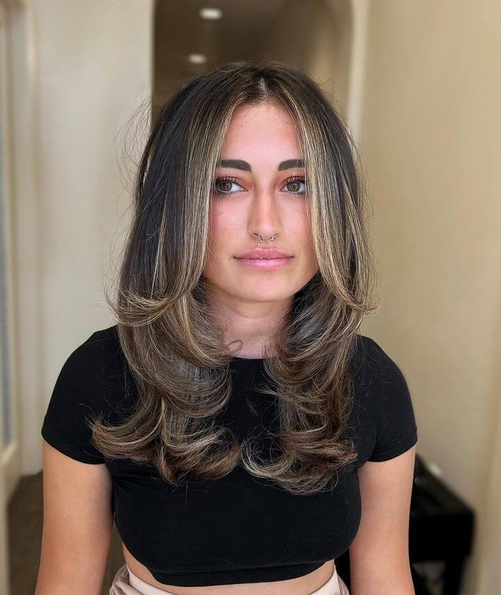 Face-framing balayage transitioning from dark roots to lighter tips, styled in gentle waves with layers