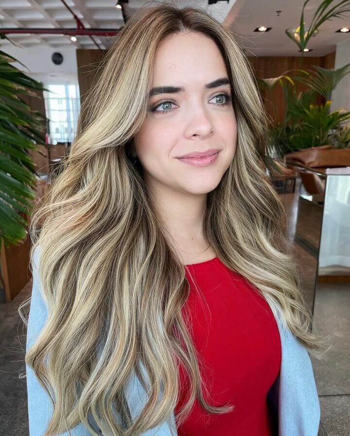 Honey-blonde balayage transitioning to lighter tips, styled in waves with long layers and a side part
