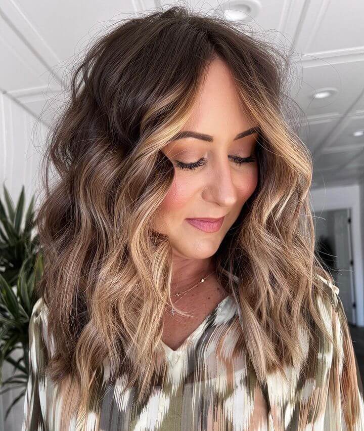 Warm honey blonde balayage from dark roots, styled in bouncy mid-length layers with soft waves