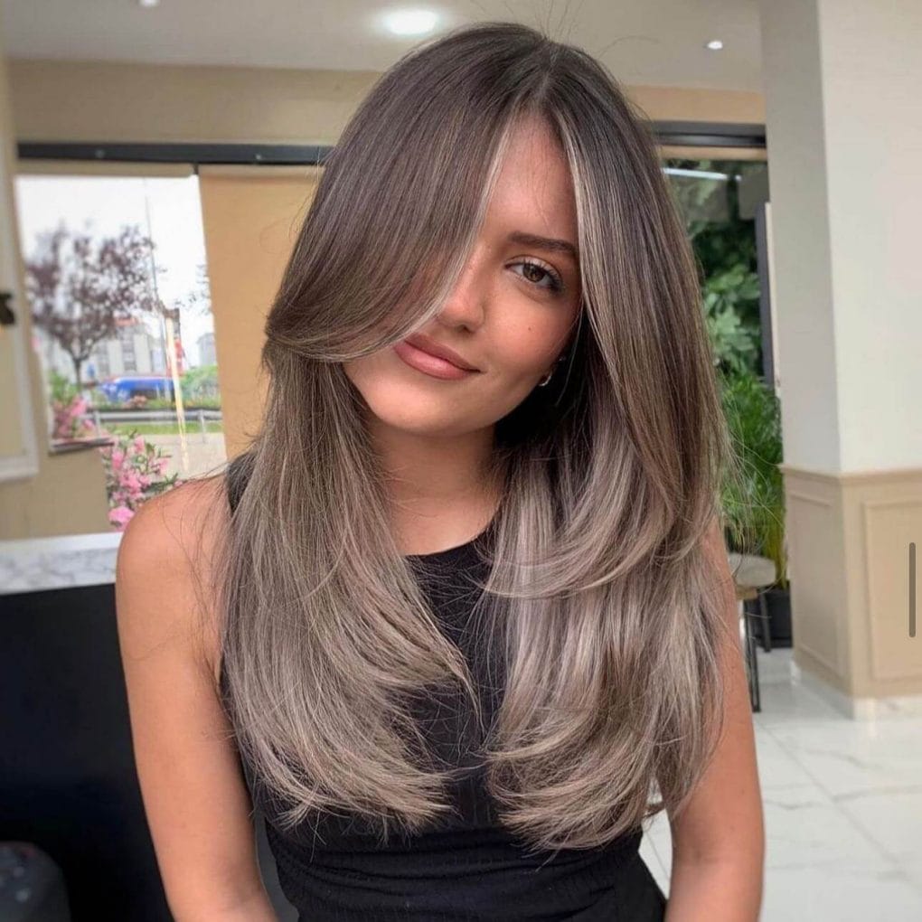 Balayage from dark brunette roots to cool ashy blonde ends, styled in smooth, straight layers
