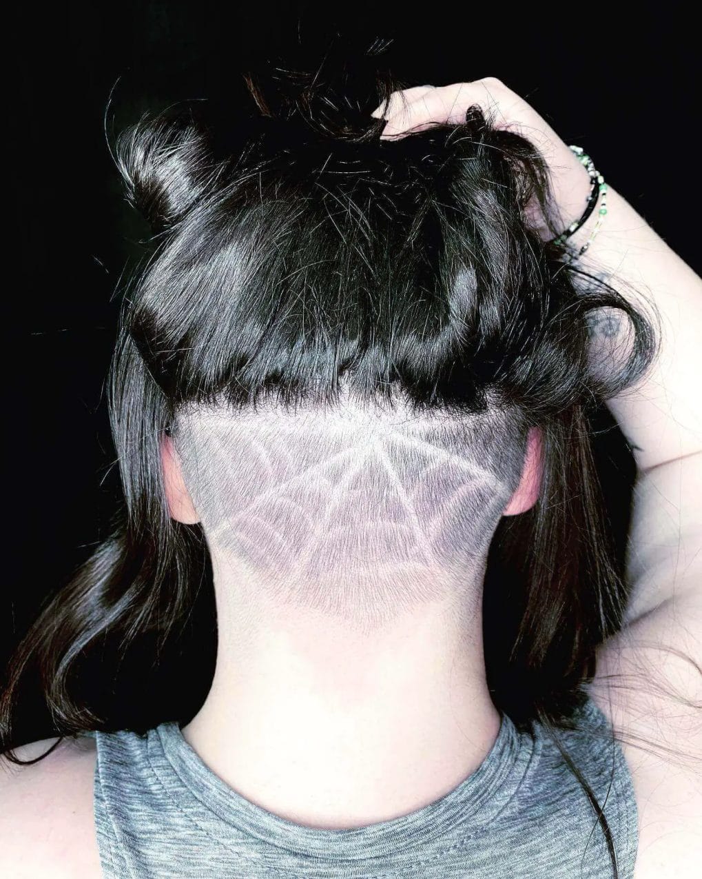 Dark hair pulled back to reveal an undercut with a web pattern.