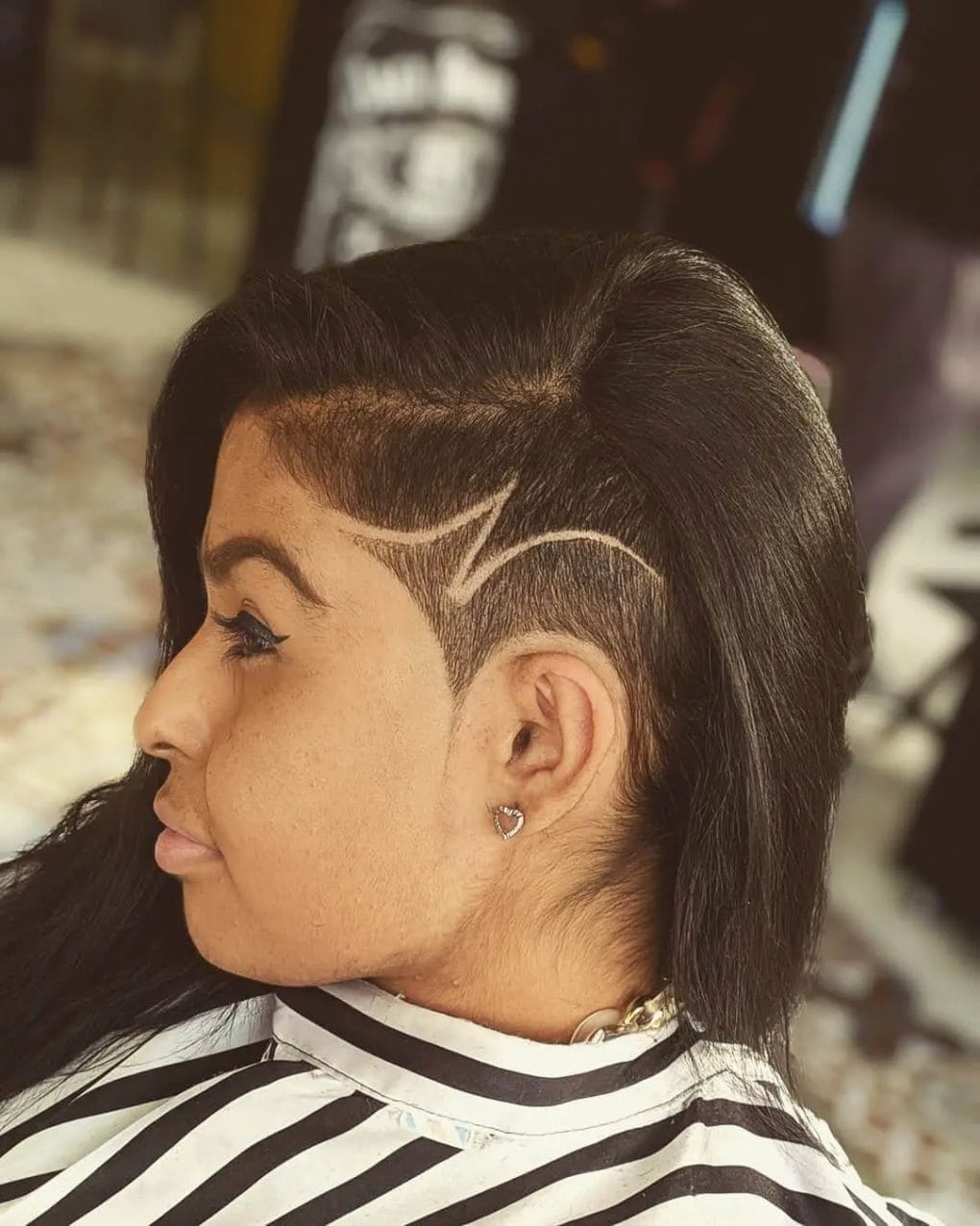 Black hair with a side-swept layer hiding a detailed undercut with curved and angular patterns.