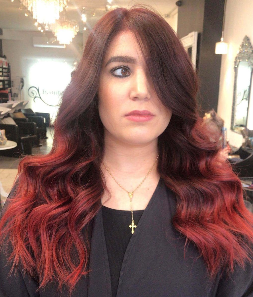 Red balayage on soft layered brunette, side-swept fringe.